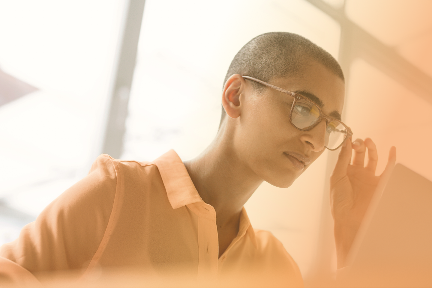 Konzentrierte Person mit Brille in orangefarbener Kleidung vor hellem Hintergrund mit Fenstern, Bild in orangefarbenem Farbverlauf gehalten.